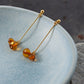 A pair of goldplated duva earrings hanging on the edge of a small blue ceramic bowl.