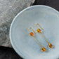 A pair of goldplated Kolga earrings laying in a small blue ceramic bowl with rocks under.