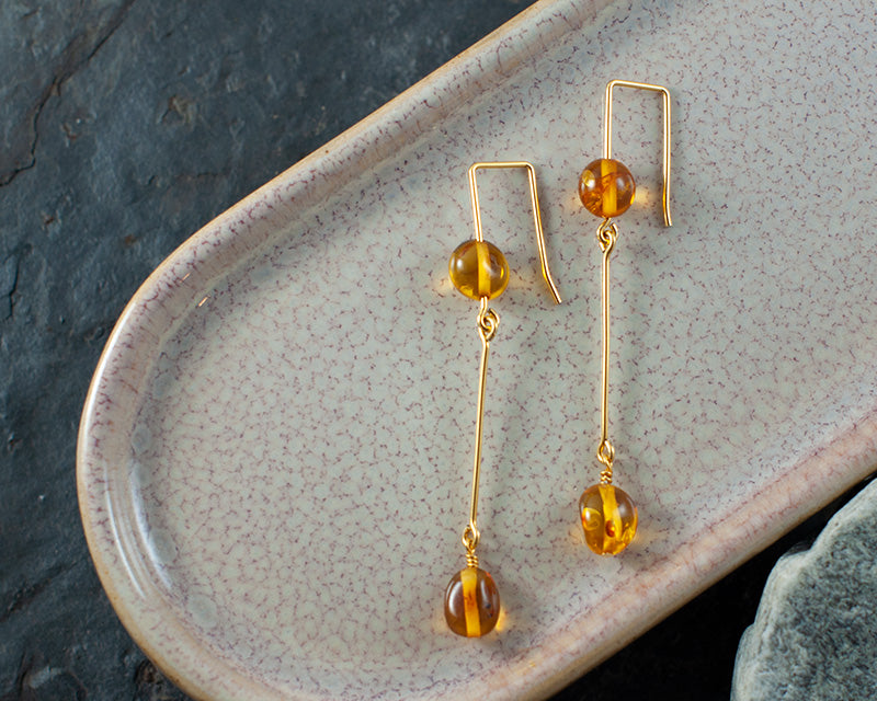 A pair of goldplated Kolga earrings laying on a ceramic plate with rocks under.