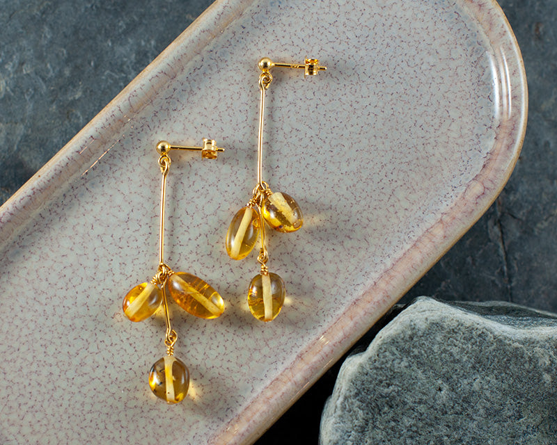 A pair of goldplated Himminglava earrings laying on a ceramic plate with rocks under.