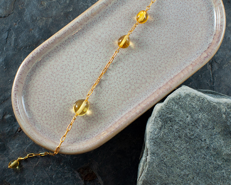 Herving goldplated bracelet laying on a ceramic plate with rocks under.